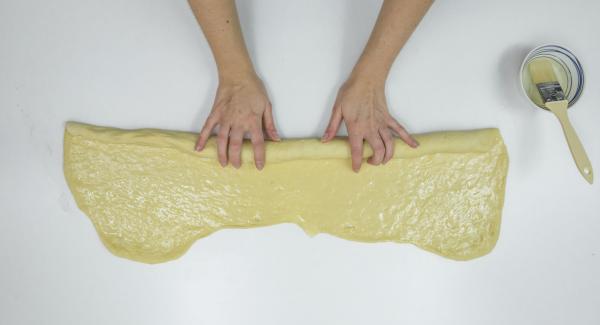 Spalmare con abbondante burro, arrotolare l'impasto partendo dal lato lungo e dargli successivamente una forma a chiocciola.