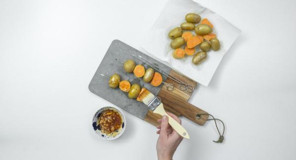 Infilare su degli spiedini le patate e i pezzi di patata dolce, alternandoli tra loro. Spennellarli leggermente con l'olio aromatizzato.