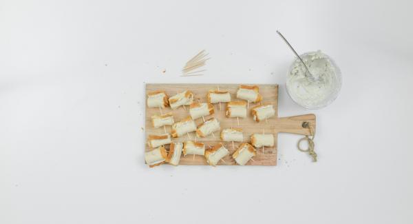 Spalmare un po’ di crema al formaggio su ciascuna striscia di pane, arrotolare e fissare con degli stuzzicadenti.