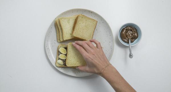 Spalmare la crema al cioccolato sulla metà delle fette di pancarrè e aggiungere dei pezzettini di banana. Coprire con le fette rimanenti.