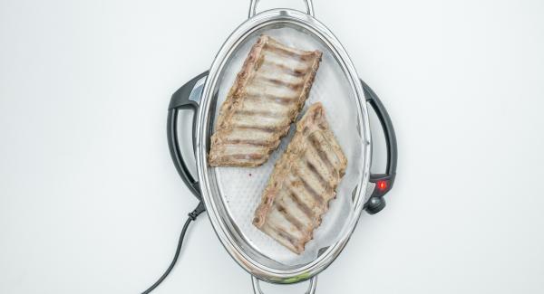 Al suono di Audiotherm, abbassare Navigenio a livello 4, posizionare la carta da forno nell’Unità Ovale Grill, disporvi le costine con la parte superiore rivolta verso il basso.