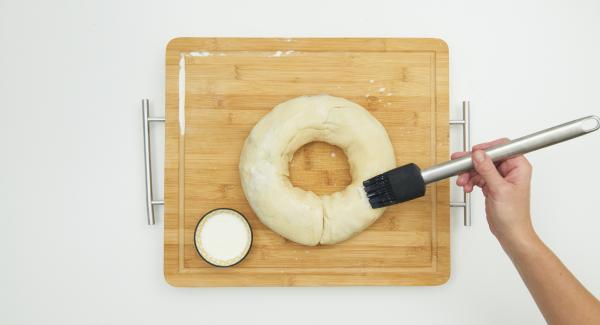 Arrotolare la pasta dal lato più lungo, formare una corona e posizionarla sulla carta da forno, nell’unità di cottura. Incidere la superficie della corona con delle forbici, spennellarla con il latte e cospargerla con la granella di zucchero e le mandorle a lamelle.